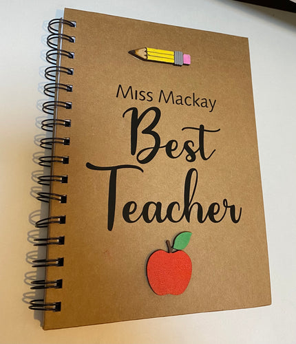 a5 kraft notebook. best teacher written on the fron in vinyl and teachers personalised name above. a hand painted wooden apple sits at the bottom and a hand painted wooden pencil at the top