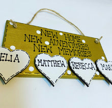 Load image into Gallery viewer, hand painted in gold this rectanglular wall plaque is 6&quot; x 3&quot;. with New home, New adventures, New memories hand written. Family Members names are written in 4cm white hearts and family pets are written on 4cm white paws. white spots pattern can be added to the gold. Hung with jute string twine
