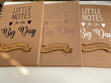 Load image into Gallery viewer, this kraft notebook is size a5. it has &quot;little noted for the big day&quot; in your choice of colour in winyl and a wooden scroll shape at the bottom with the couples names hand written
